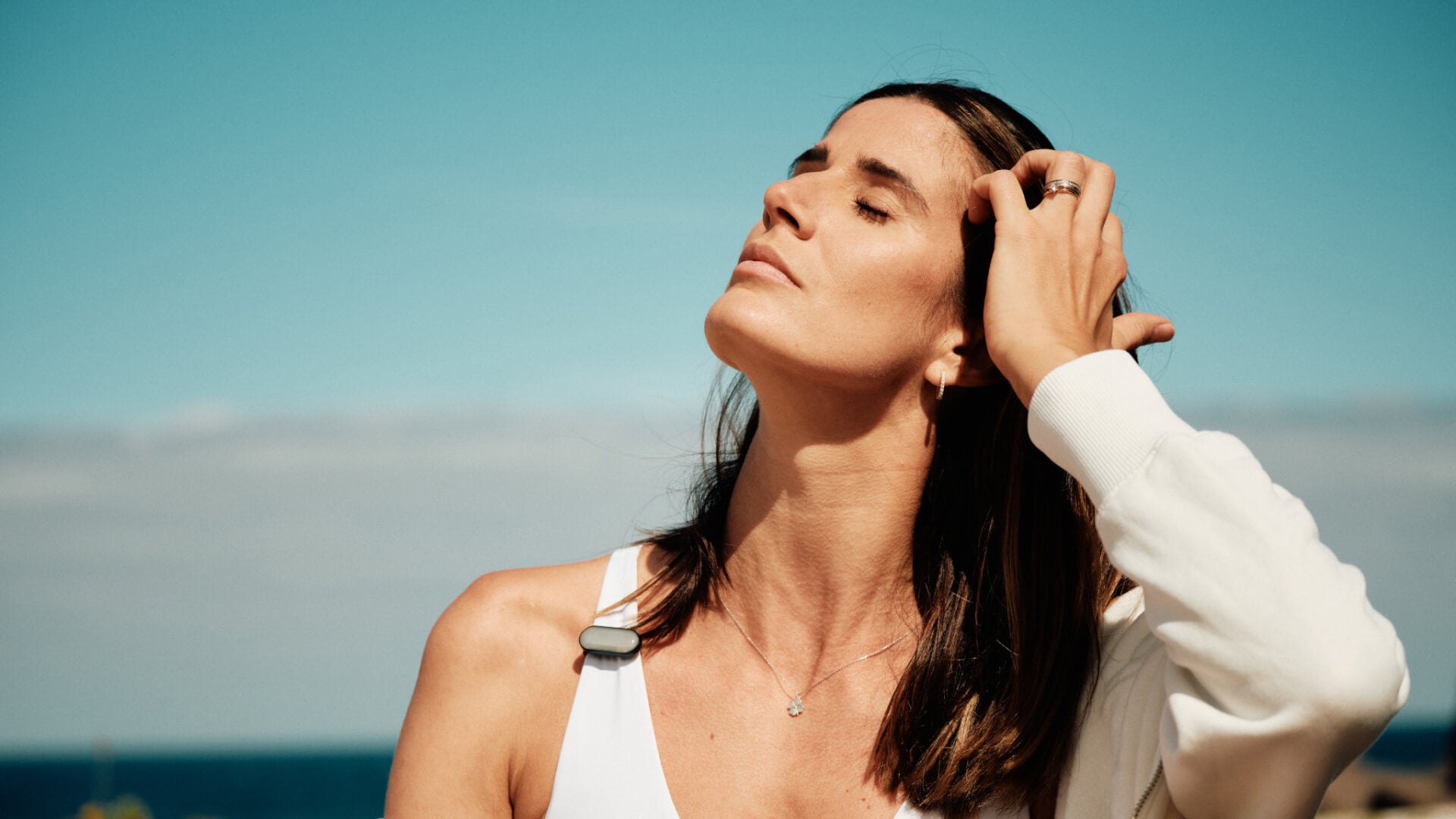 Close-up of woman wearing white tank top with sun-a-wear UV tracker attached to the strap as part of her apparel 