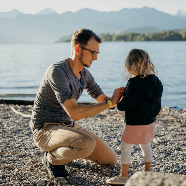 Father and daughter enjoying sunny day on a lake beach, father attaching UV tracker to daughter's clothes